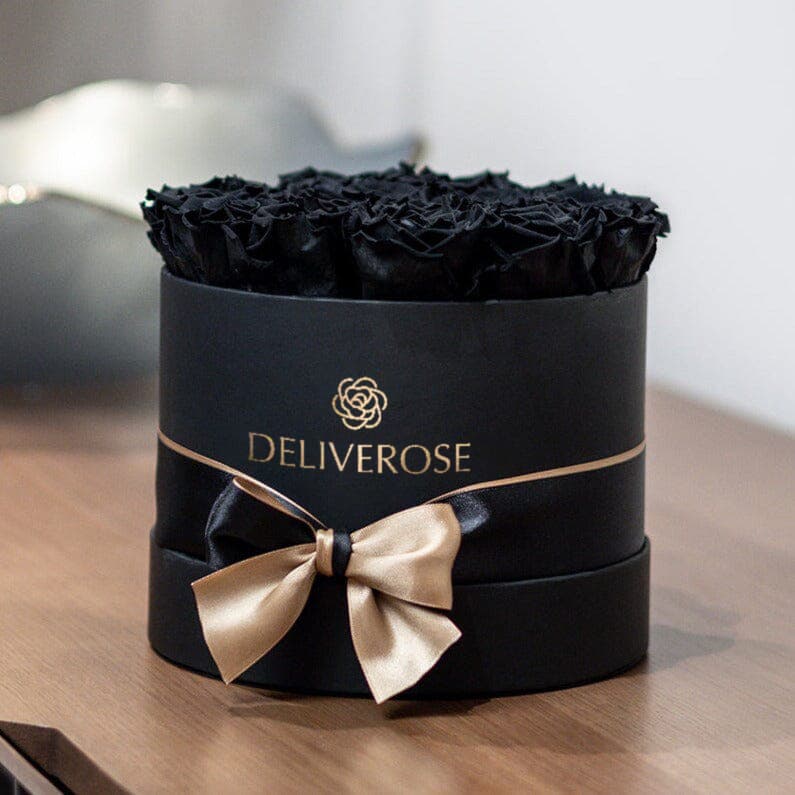 A black Deliverose box of black preserved roses with a champagne bow, on a dark wooden surface